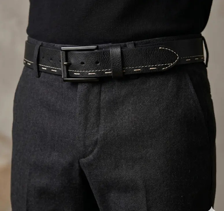 Black leather belt with a large buckle worn by a person in dark pants against a neutral background