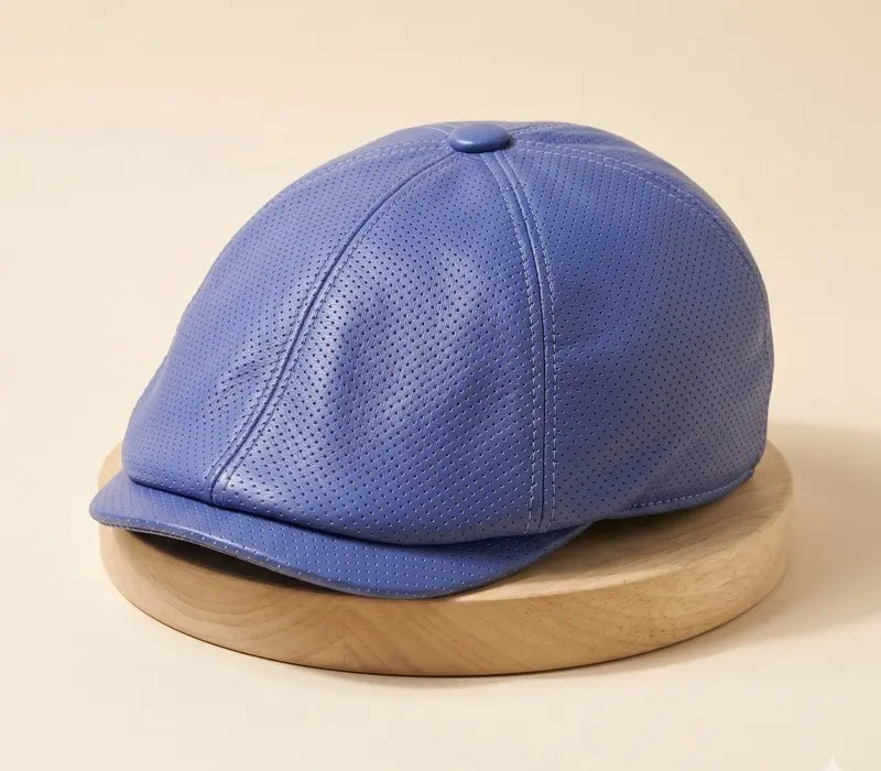 Blue perforated mix leather handmade peaked cap on a wooden stand against a beige background