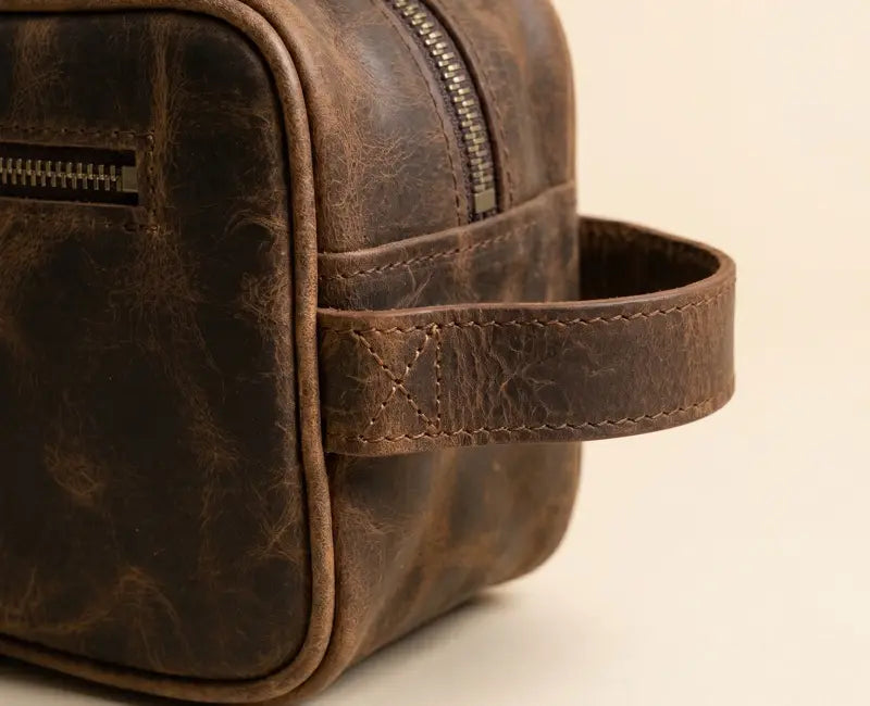 Brown leather dopp kit with handle on a beige background