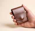 Hand holding a brown leather wallet against a beige background