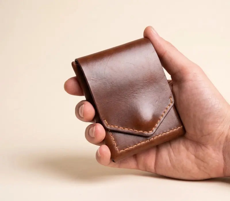 Hand holding a brown leather wallet against a beige background
