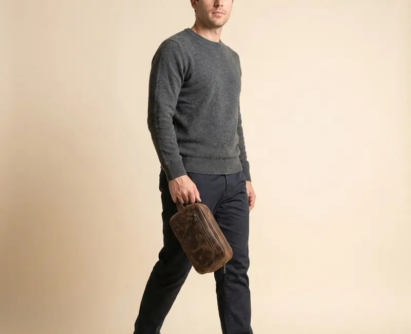 Man holding a brown leather bag against a beige background