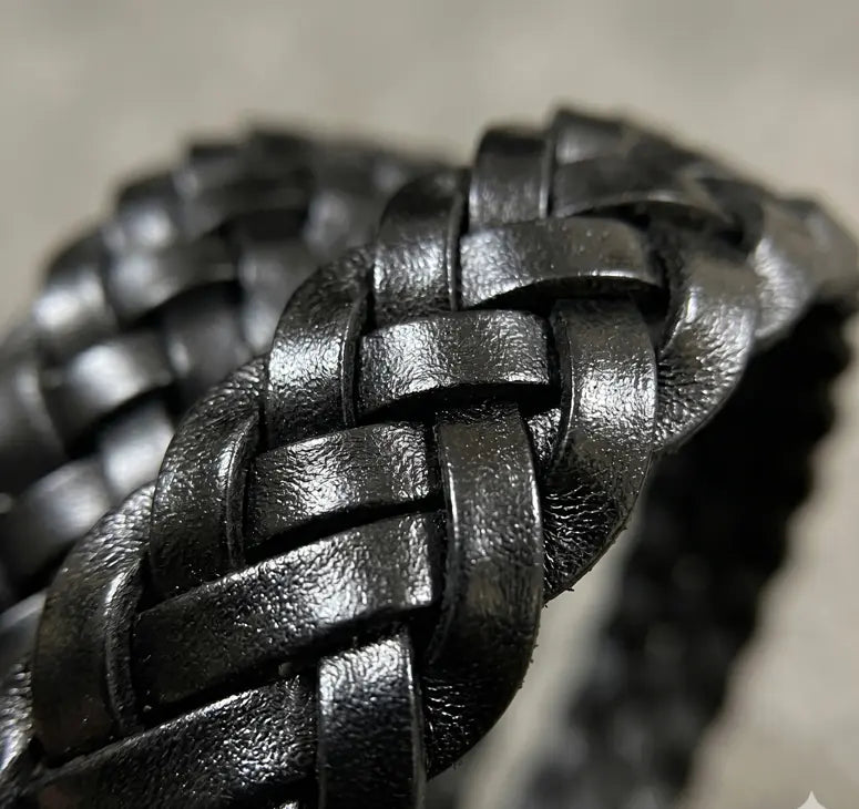 Close-up of a braided black leather bracelet on a neutral background
