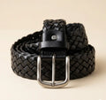 Black woven belt with a silver buckle on a beige background