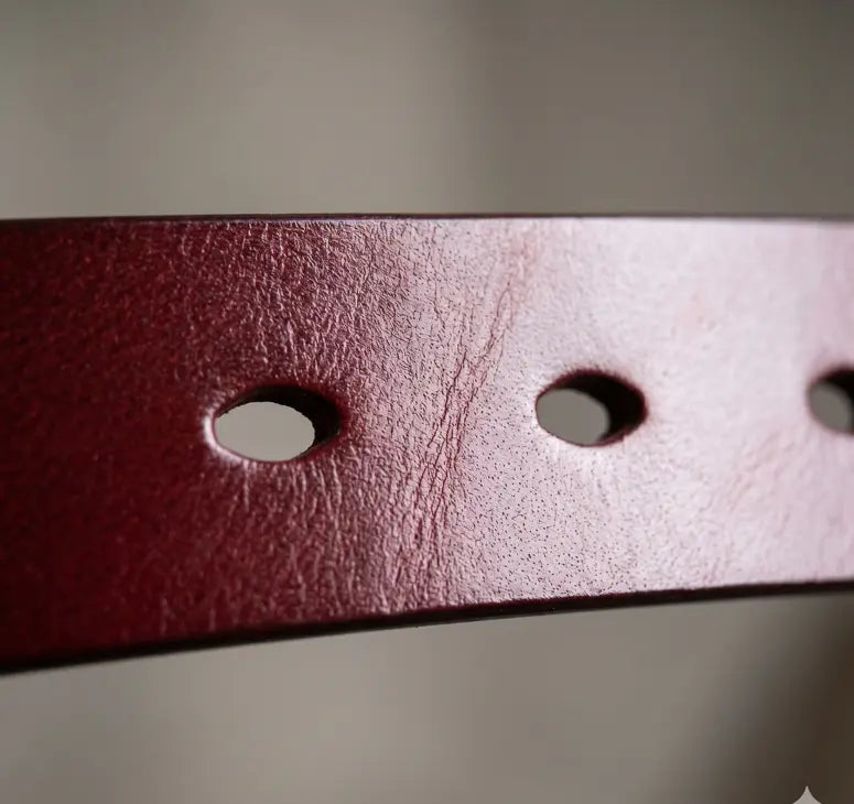 Close-up of a leather belt with three holes on a neutral background