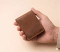 Hand holding a brown leather wallet against a beige background