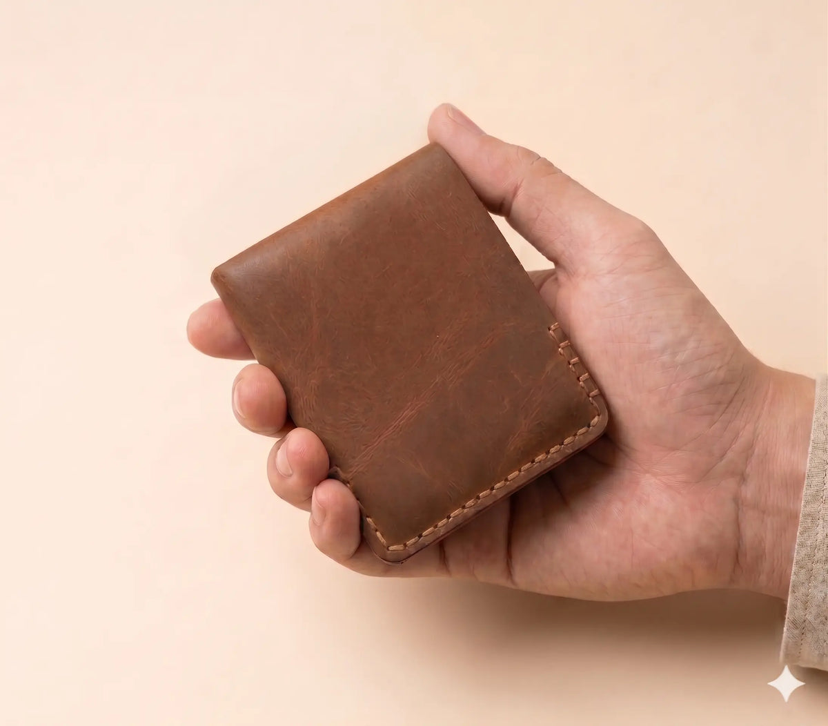 Hand holding a brown leather wallet against a beige background