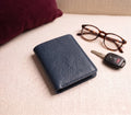 Blue leather wallet, glasses, and car key on a beige surface