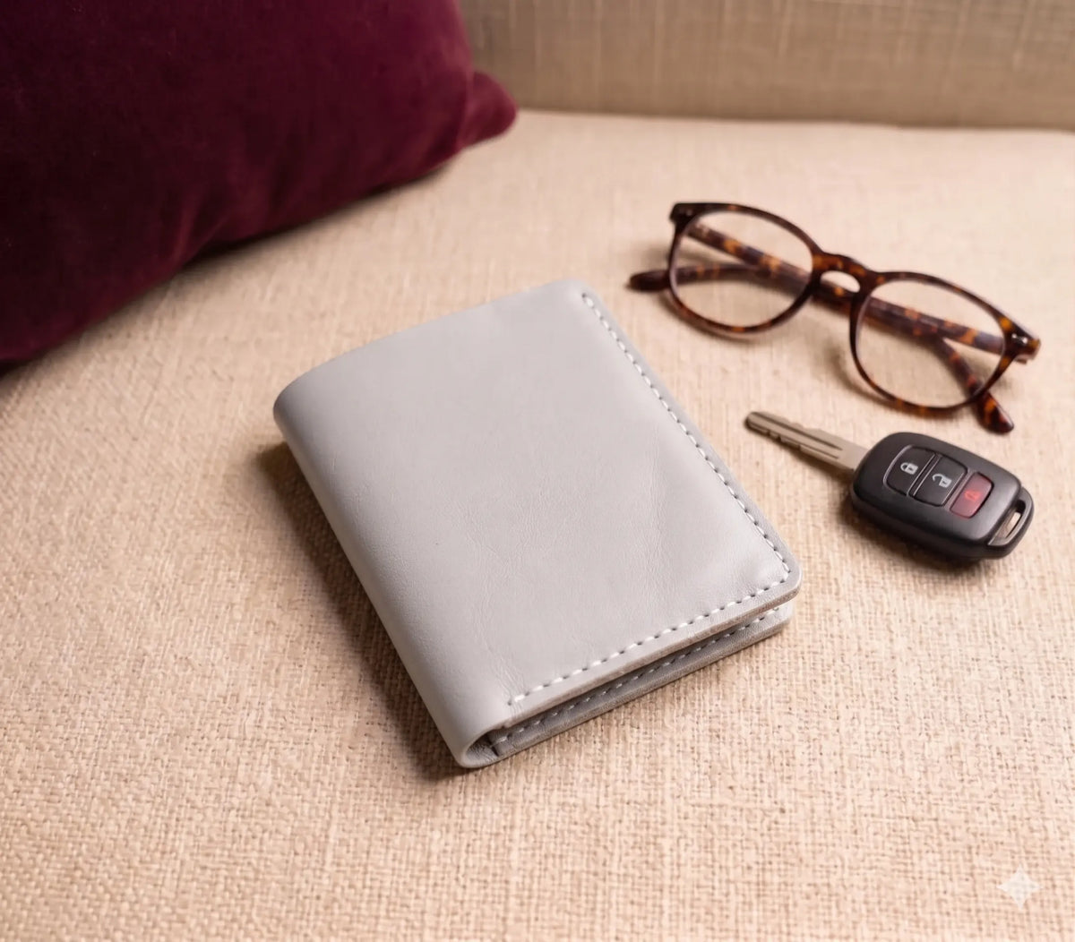 Gray wallet, glasses, and car key on a beige surface